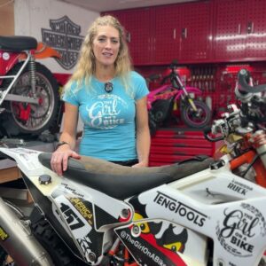 Vanessa Ruck smiling behind her rally motorcycle in her home workshop