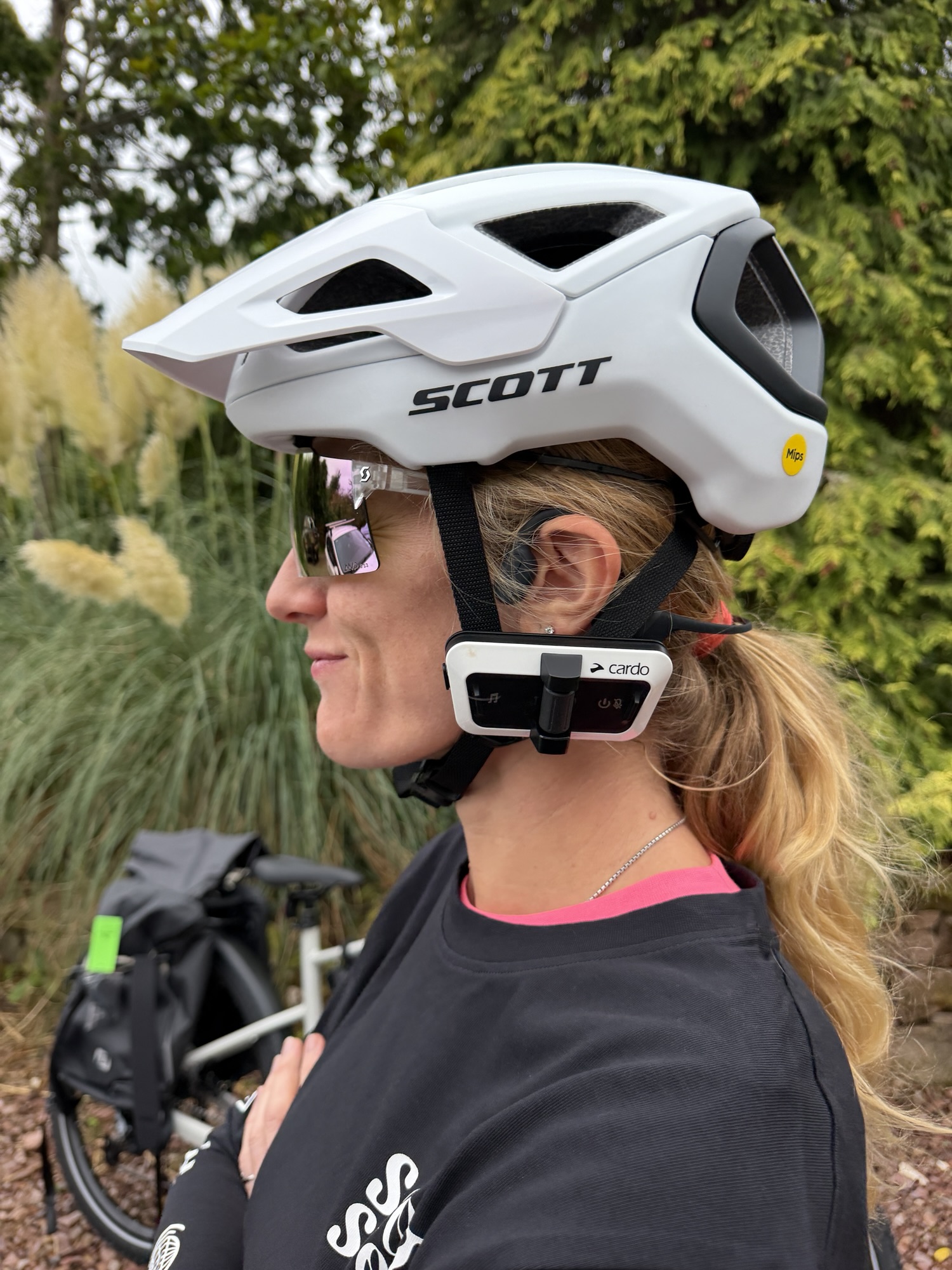Side view of a cyclist wearing a SCOTT helmet with a Cardo intercom mounted beside the helmet strap.