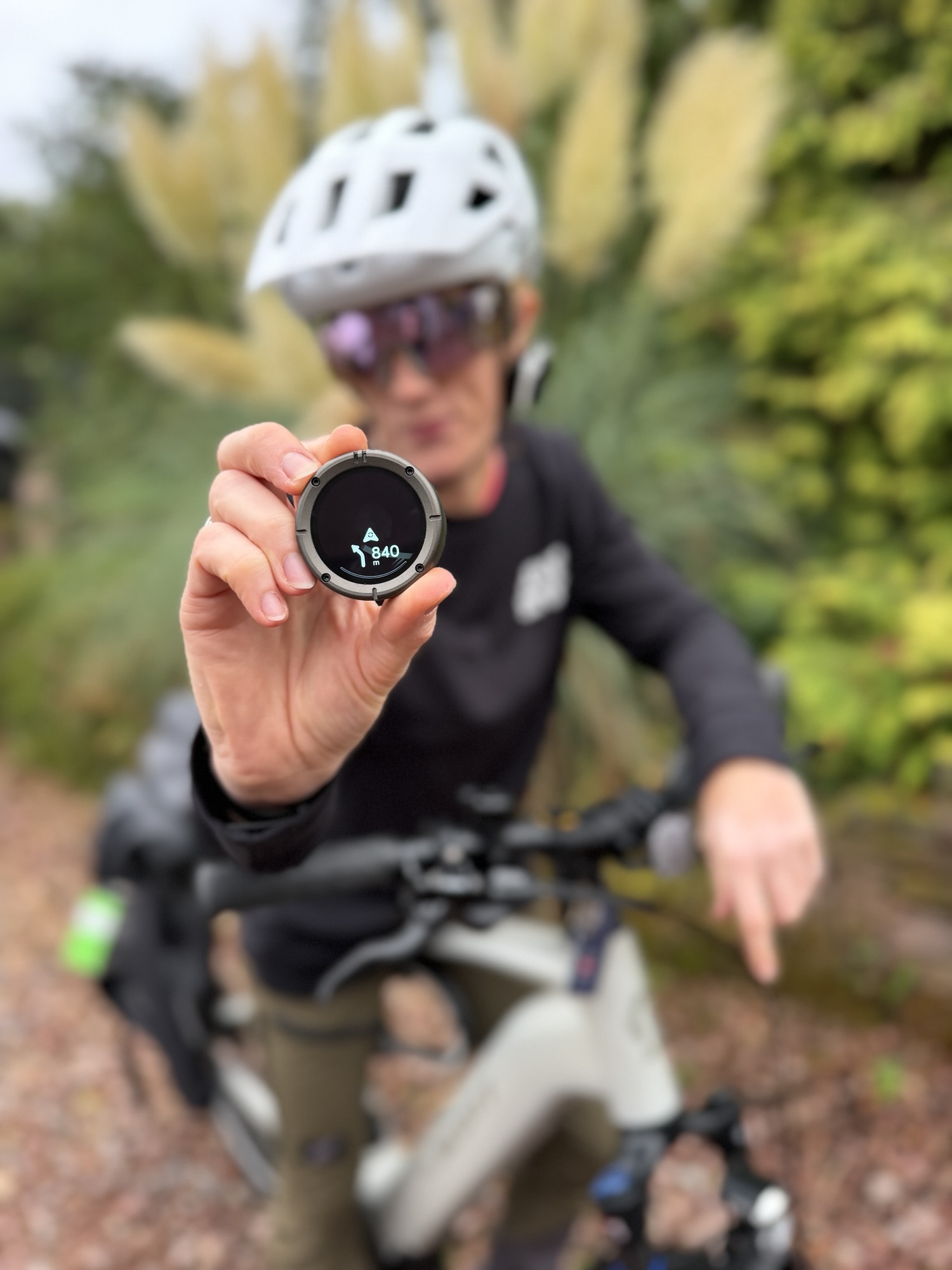 A helmeted cyclist holding a round Beeline navigation device towards the camera.